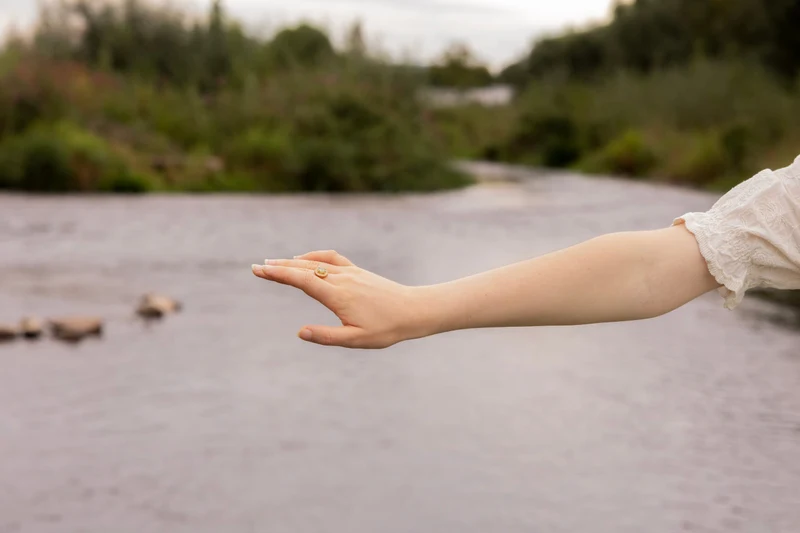 Ausgestreckter Arm mit Ring über dem ruhigen Wasser des Flusses
