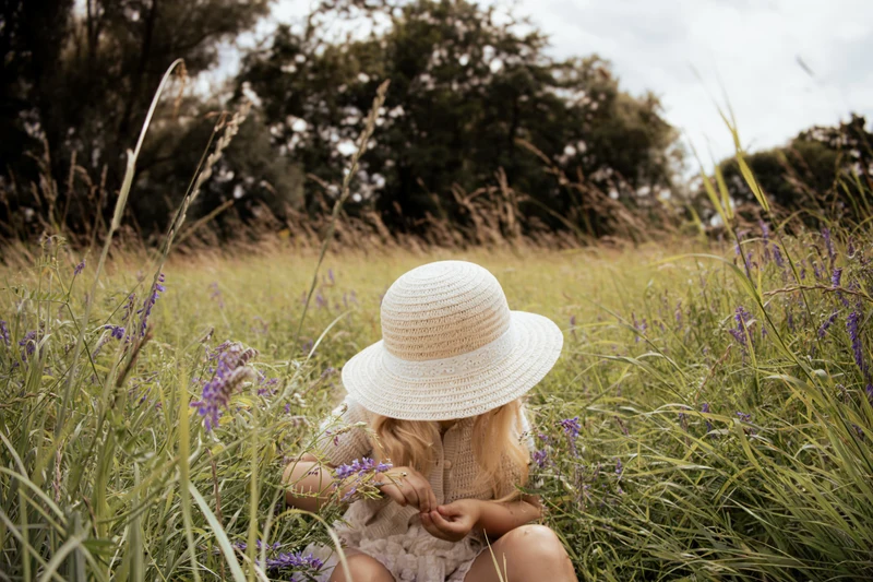 Kind mit Strohhut sitzt zwischen lila Wildblumen