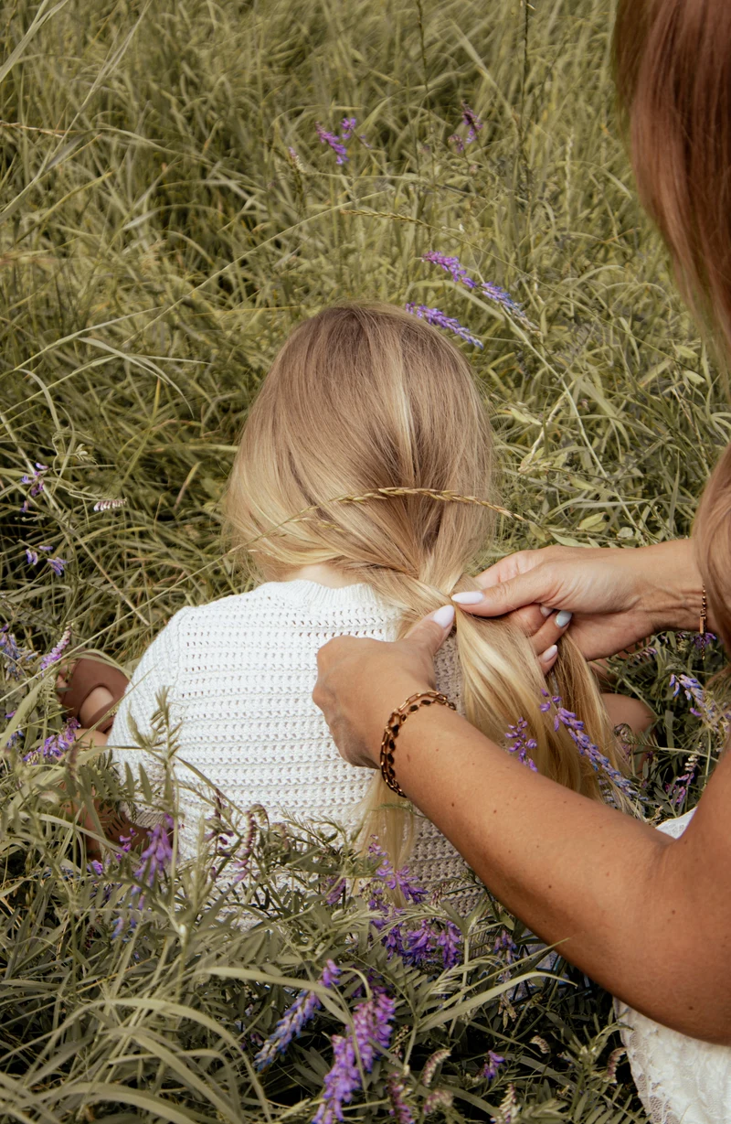Mutter flechtet ihrer Tochter die Haare in der Wiese